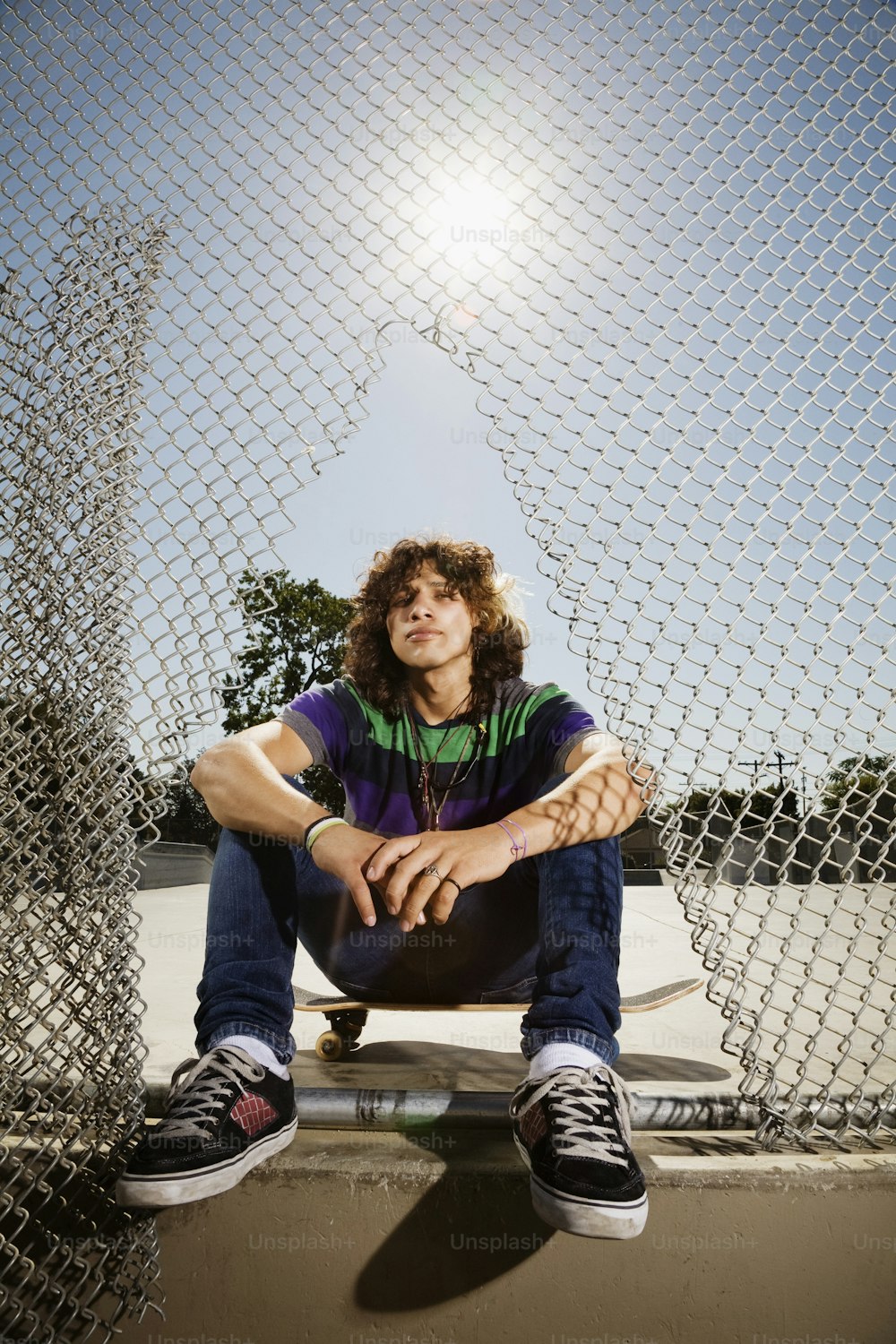 Ein Mann sitzt auf einem Skateboard vor einem Zaun