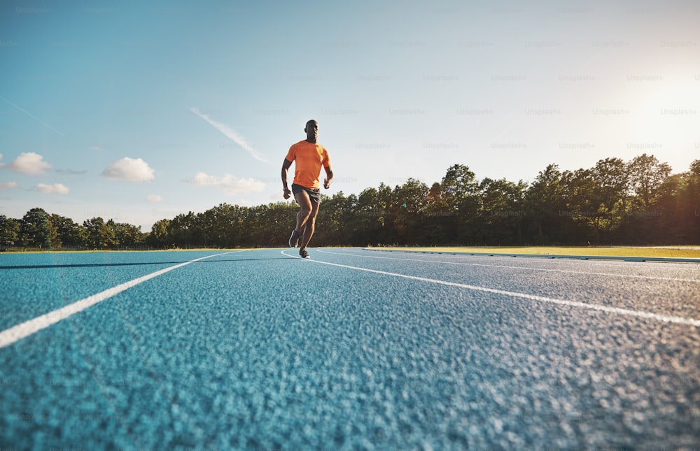 Fokussierter junger afrikanischer männlicher Athlet in Sportbekleidung, der an einem sonnigen Tag alleine auf einer Laufstrecke rennt