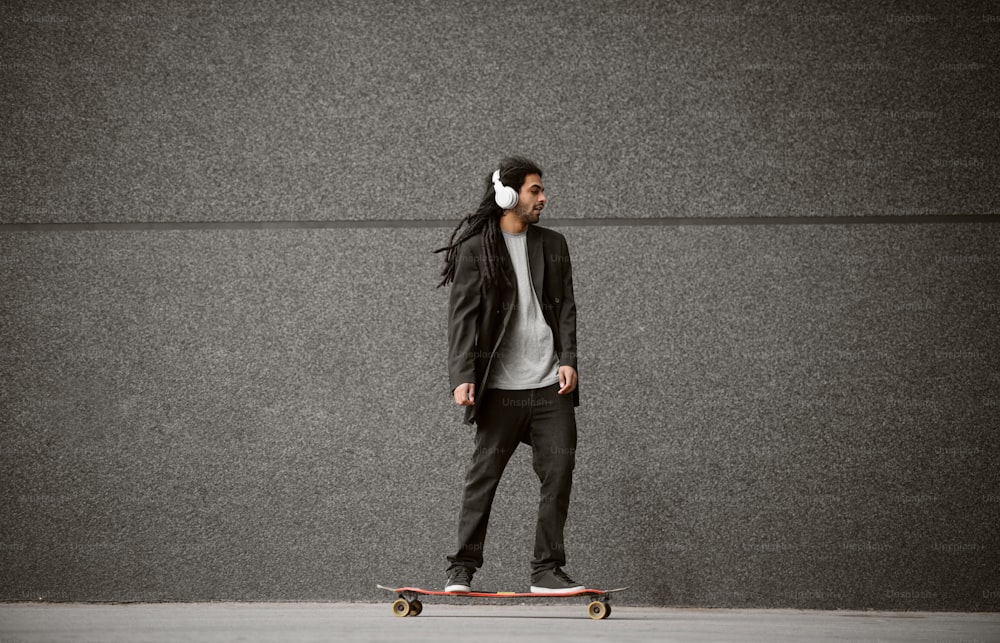Close up de elegante homem skatista dreadlocks feliz feliz em um terno de pé no skate enquanto ouve música na rua.