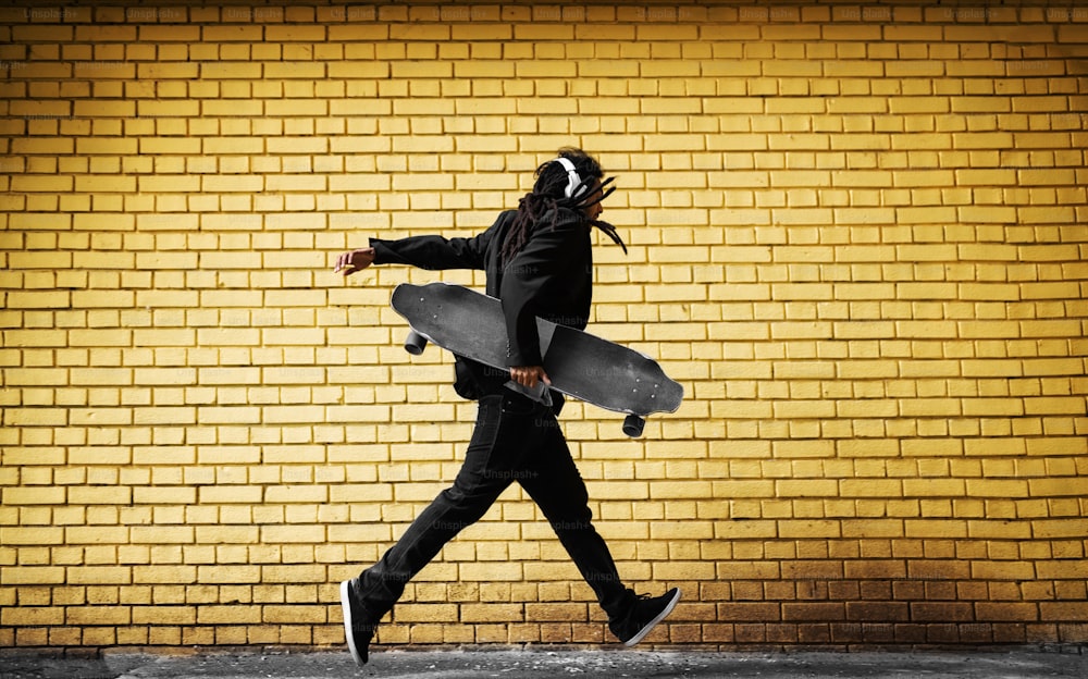 잘생긴 젊은 향취 스케이터가 거리의 노란 벽 근처에서 정장을 입고 헤드폰을 끼고 있습니다.