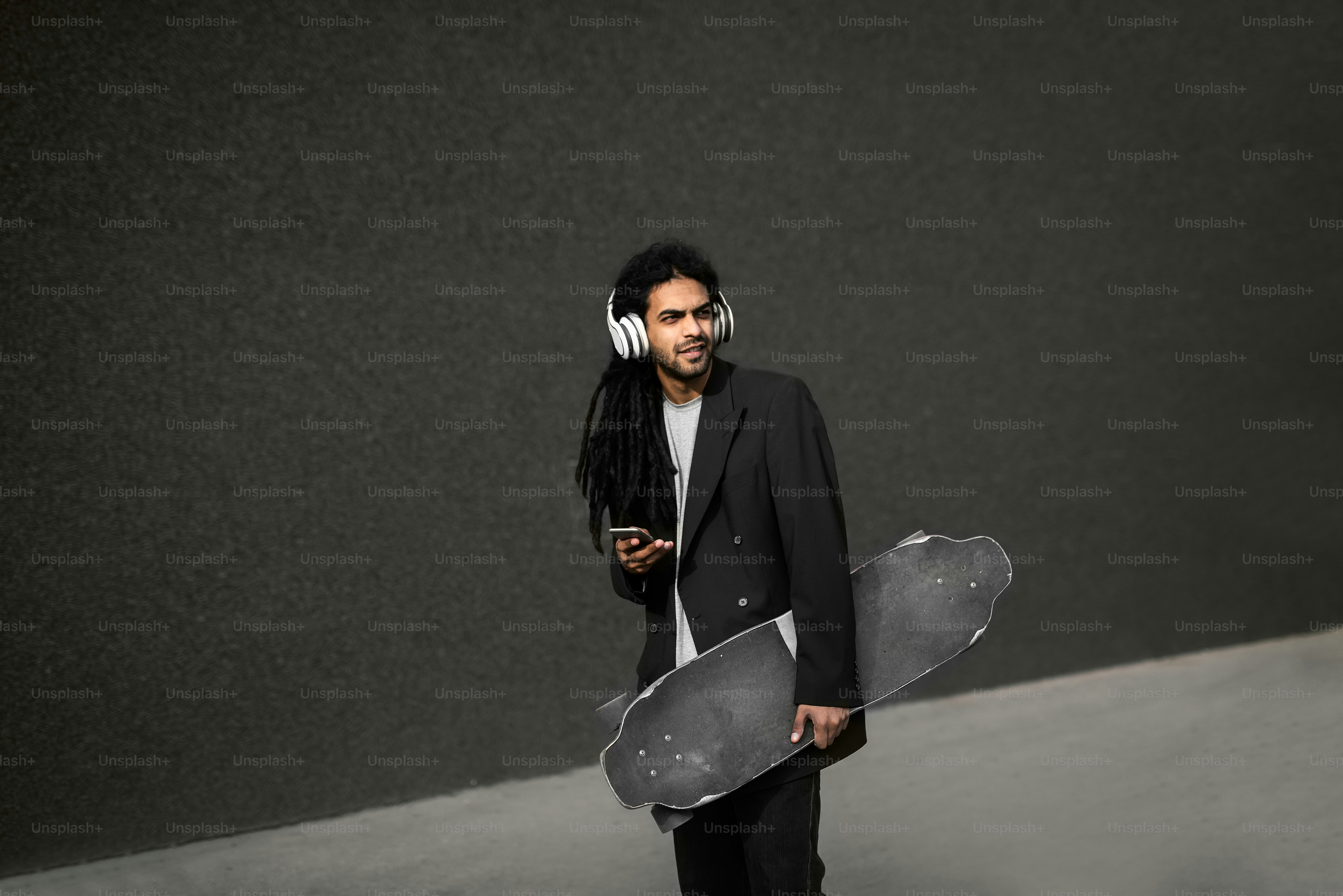 Stylish young dreadlocks hipster skater with headphones listening music holding smart phone.