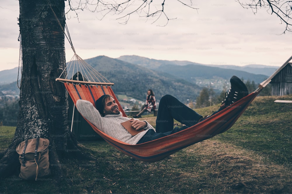 Handsome young man lying in hammock and smiling while camping with his girlfriend
