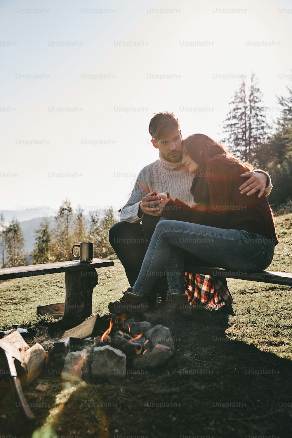 Beautiful young couple having morning coffee while sitting by the campfire in mountains