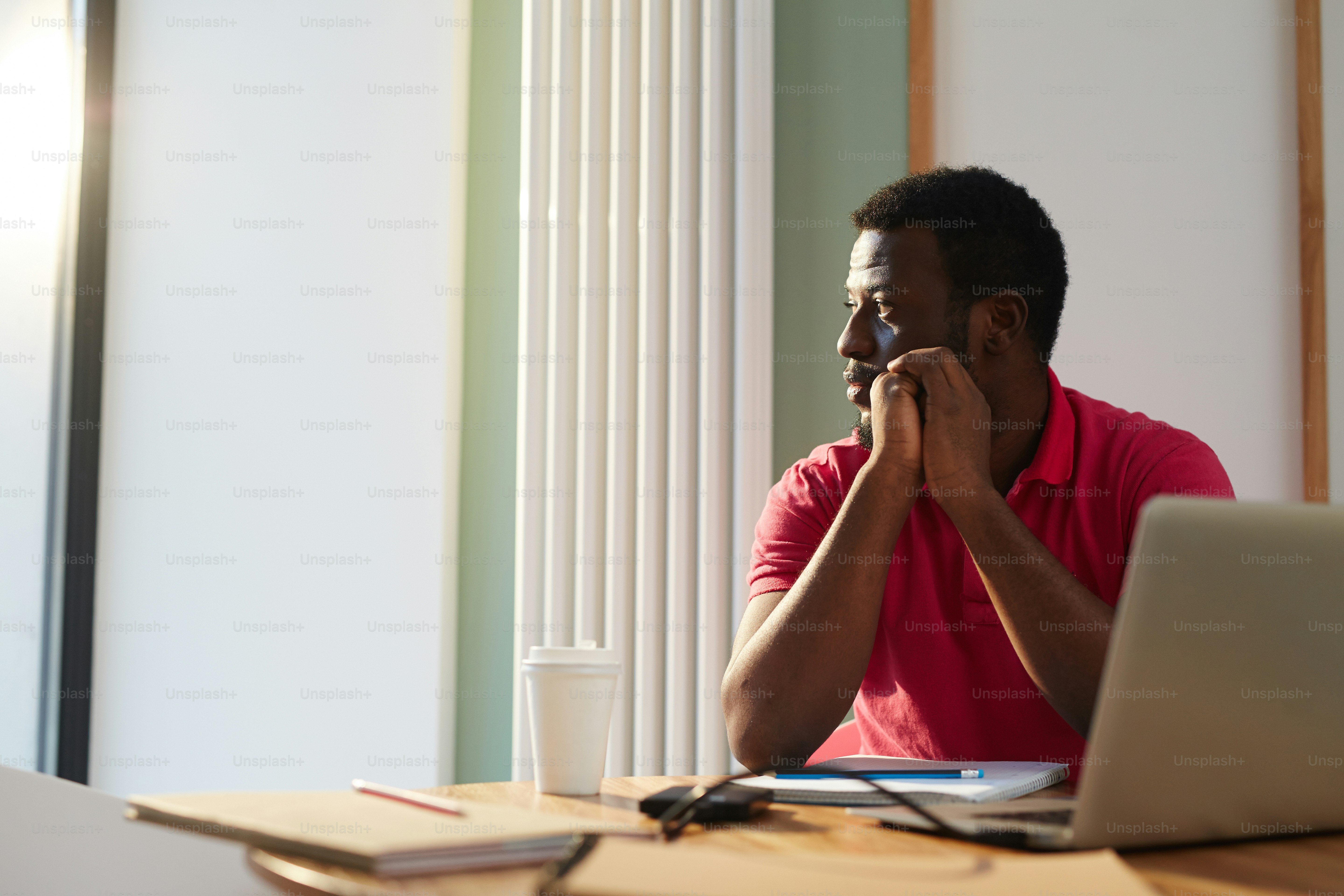 Dipendente pensieroso che guarda attraverso la finestra in una giornata di sole mentre è seduto alla scrivania in ufficio
