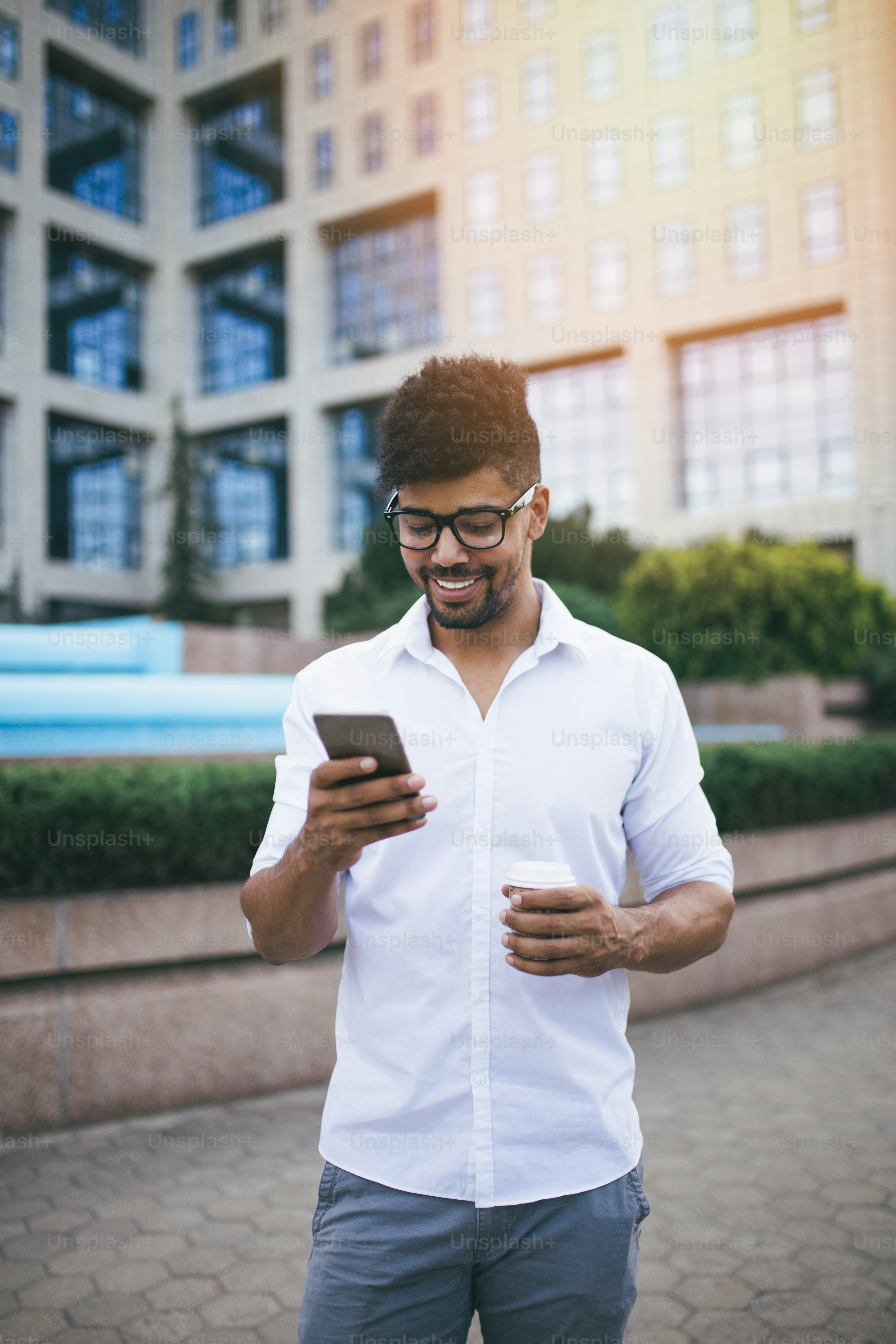 Young handsome Afro American man standing in front of huge modern business building smiling and talking on cell phone.