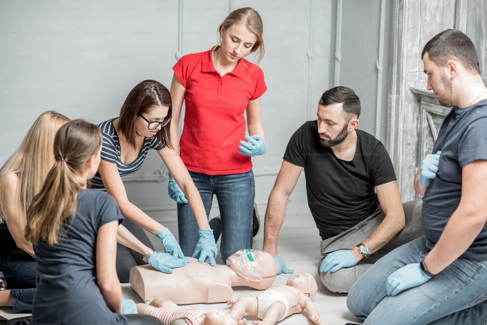 Group of people learning how to make first aid heart compressions with dummies during the training indoors