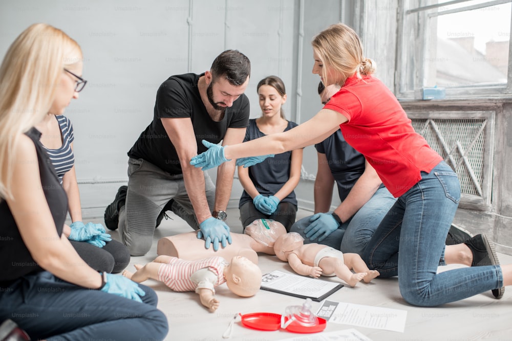 Young woman instructor helping to make first aid heart compressions with dummy during the group training indoors