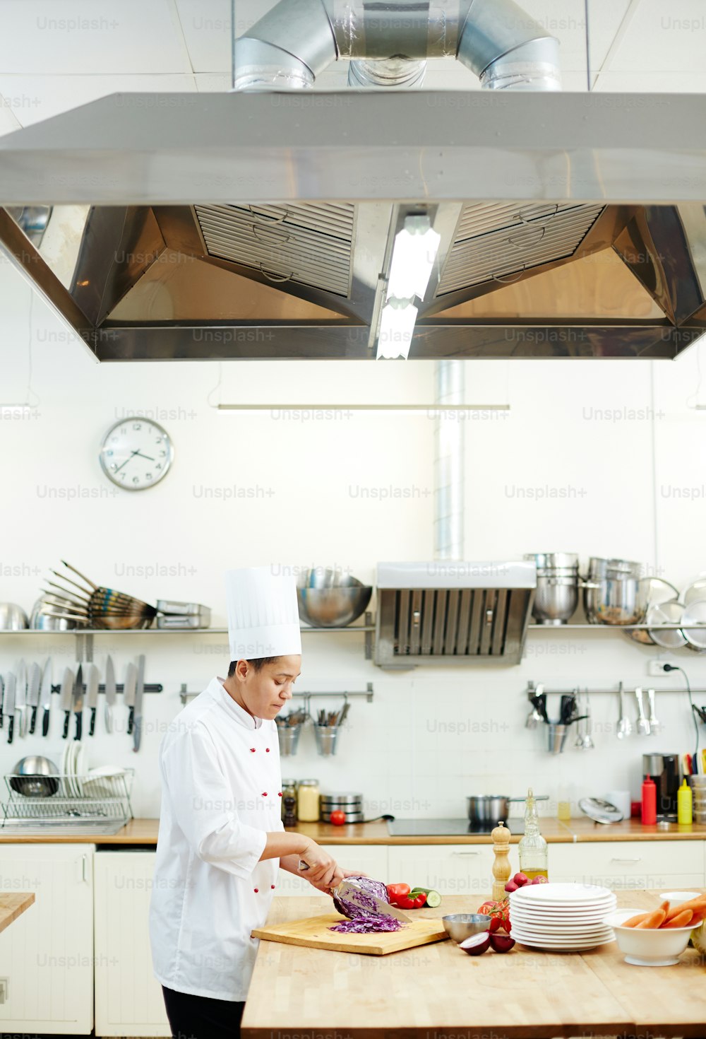 Jeune femme en uniforme de chef debout à table et coupant des ingrédients pour le ragoût de légumes