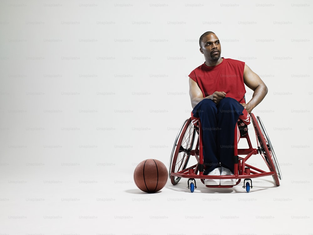 um homem sentado em uma cadeira de rodas ao lado de uma bola de basquete