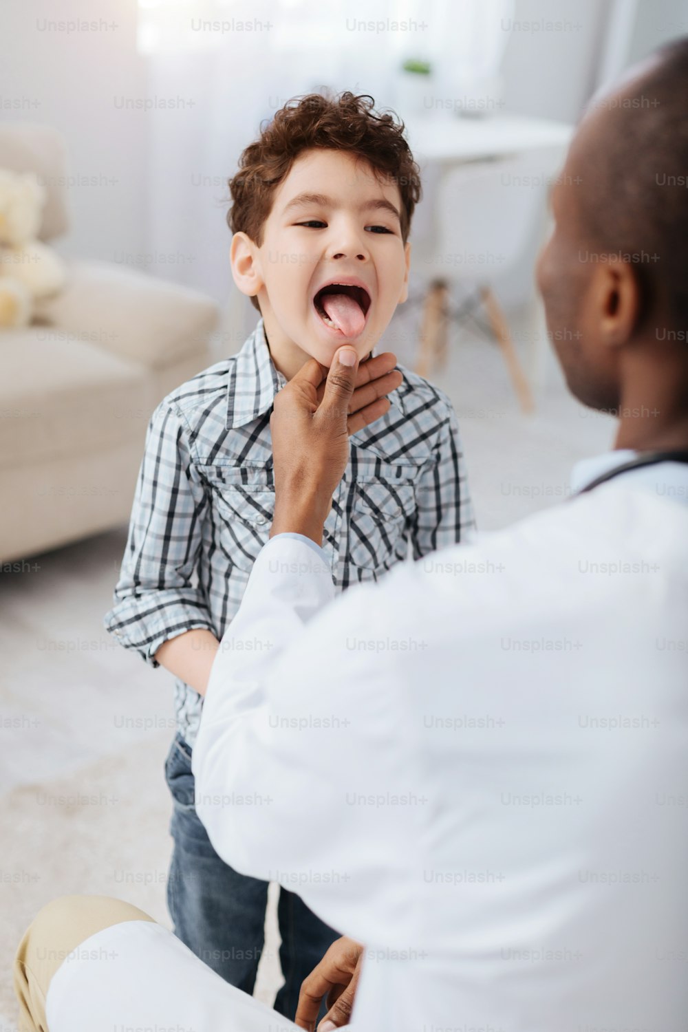 Erkältungssymptome. Energisch ansprechender Junge, der steht, während er Zunge demonstriert und männlicher Arzt sein Kinn berührt