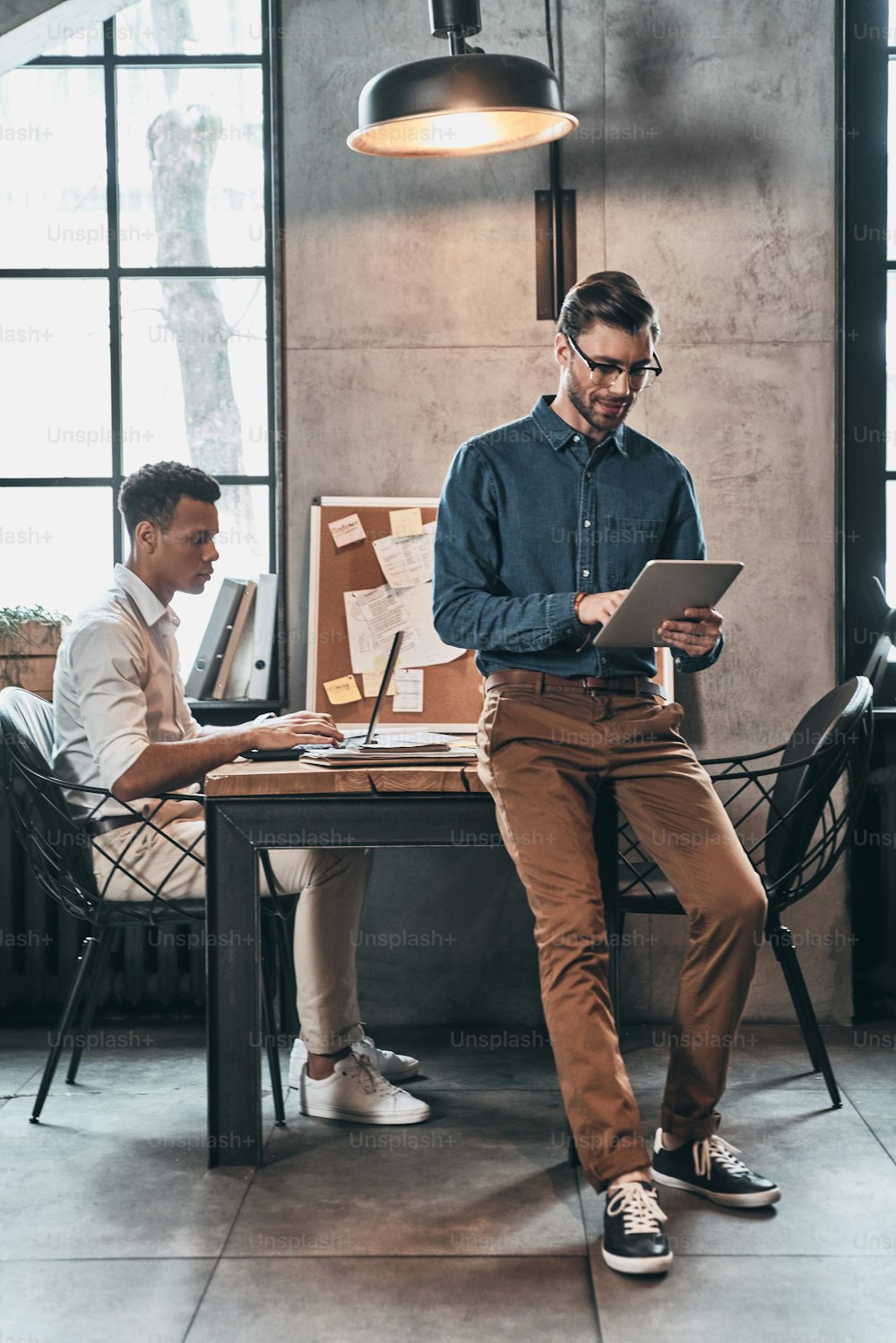 Dois homens confiantes em roupas casuais inteligentes concentrando-se no trabalho enquanto passam o tempo no escritório
