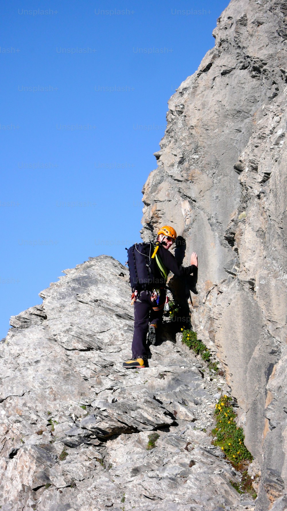 A male mountain climber at the start of a long climbing route under a clear blue sky