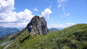 草が茂った尾根を登る途中、背後に素晴らしい山の風景が広がる登山ルートを登る男性登山者