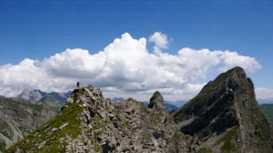 Un escalador masculino en una cresta cubierta de hierba en su camino hacia abajo de una ruta de escalada con un gran paisaje montañoso detrás de él
