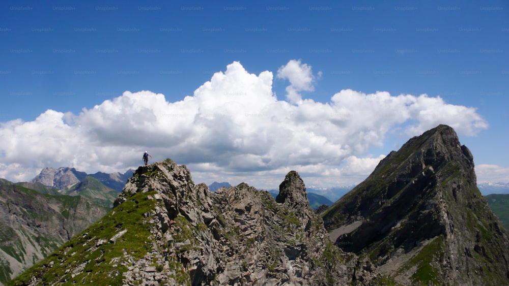 Ein männlicher Kletterer auf einem grasbewachsenen Grat auf dem Weg von einer Kletterroute mit einer tollen Berglandschaft im Rücken