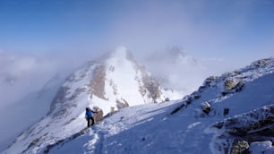 Un esquiador de travesía masculino caminando a una cumbre alpina alta en Suiza a lo largo de una cresta de roca y nieve en una ligera niebla