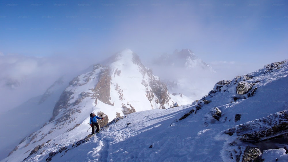 A male backcountry skier hiking to a high alpine summit in Switzerland along a rock and snow ridge in light fog
