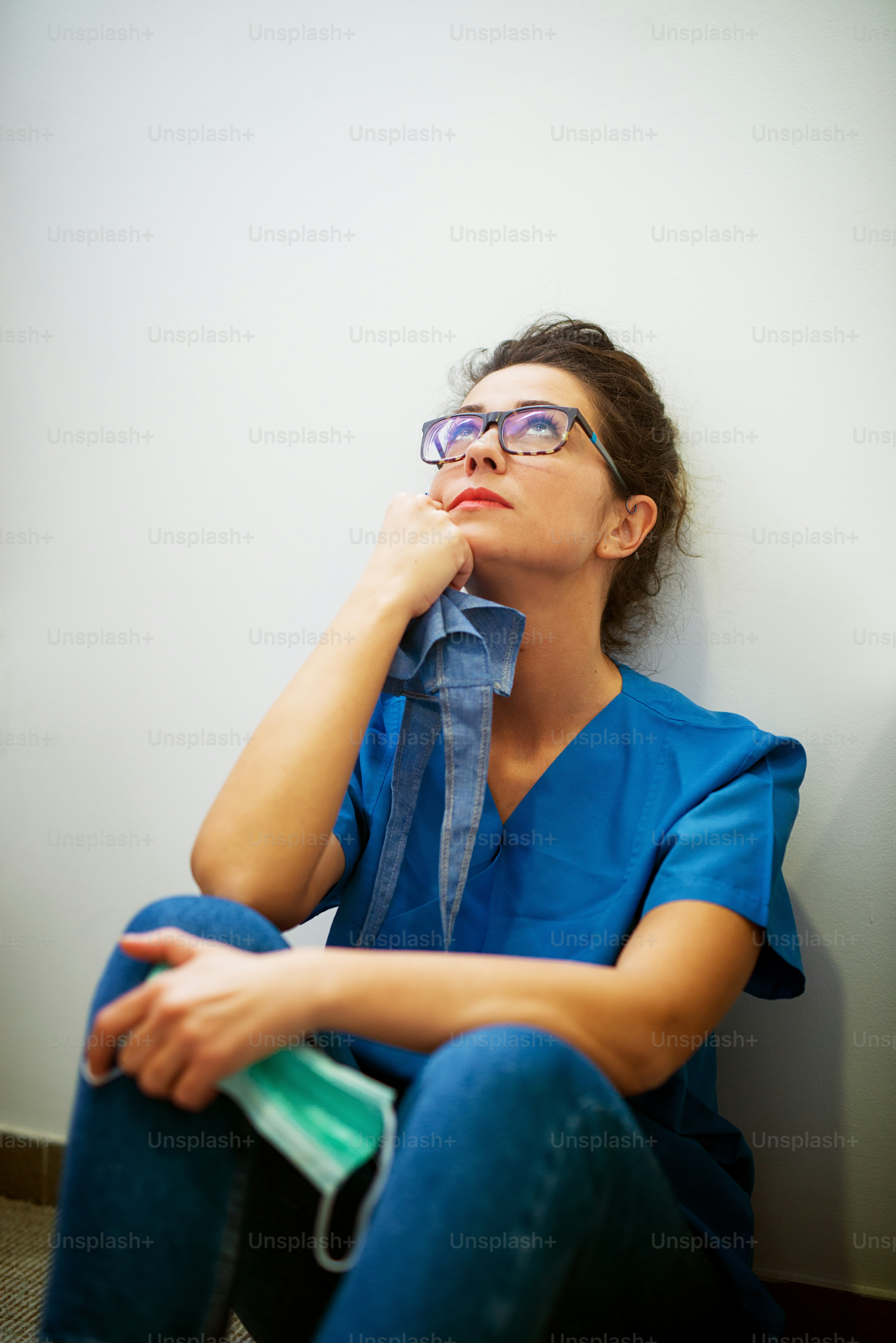 Portrait of middle age woman surgeon sitting on the floor leaned on the wall after an operation and praying by looking up.