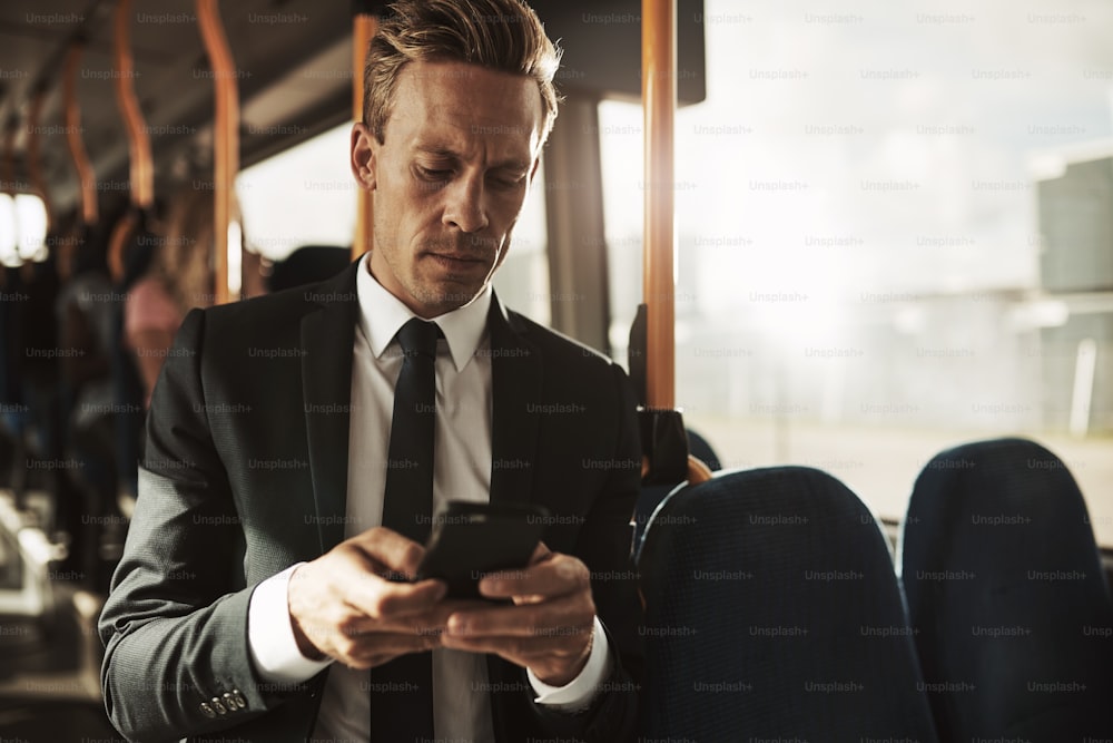 Focused young businessman wearing a suit standing on a bus during his morning commute reading text messages