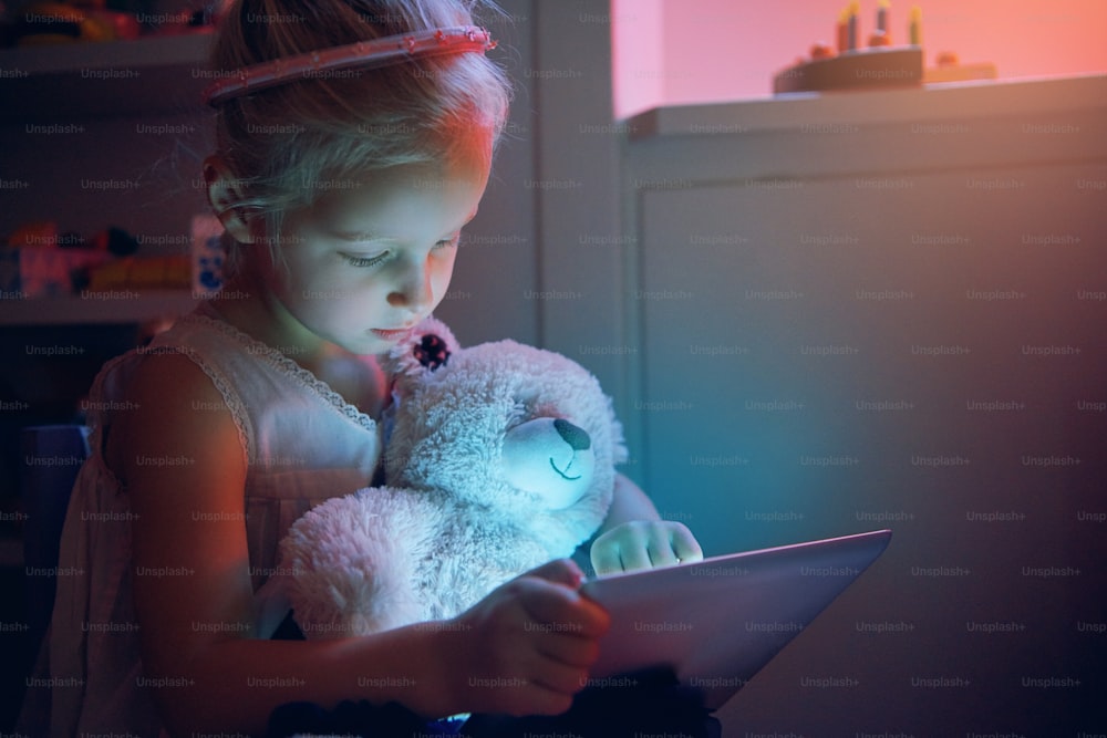 Little girl with bear using tablet. Horizontal indoors shot.