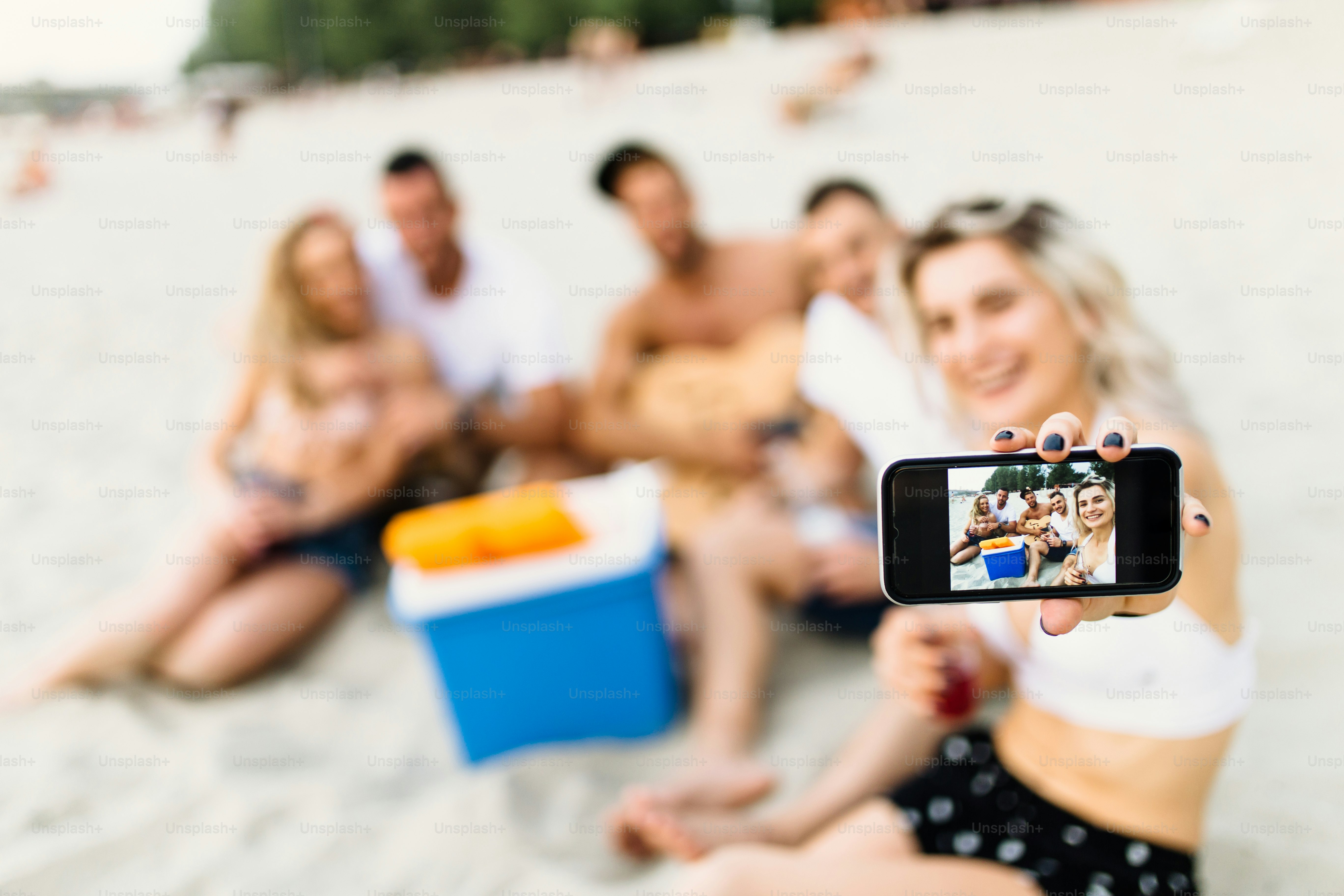 Groupe de jeunes gens attrayants profitant à la plage, buvant, trinquant et faisant un selfie avec un téléphone intelligent