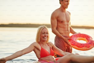 Smiling young woman in a bikini floating on a ring while enjoying a day at a lake with her boyfriend