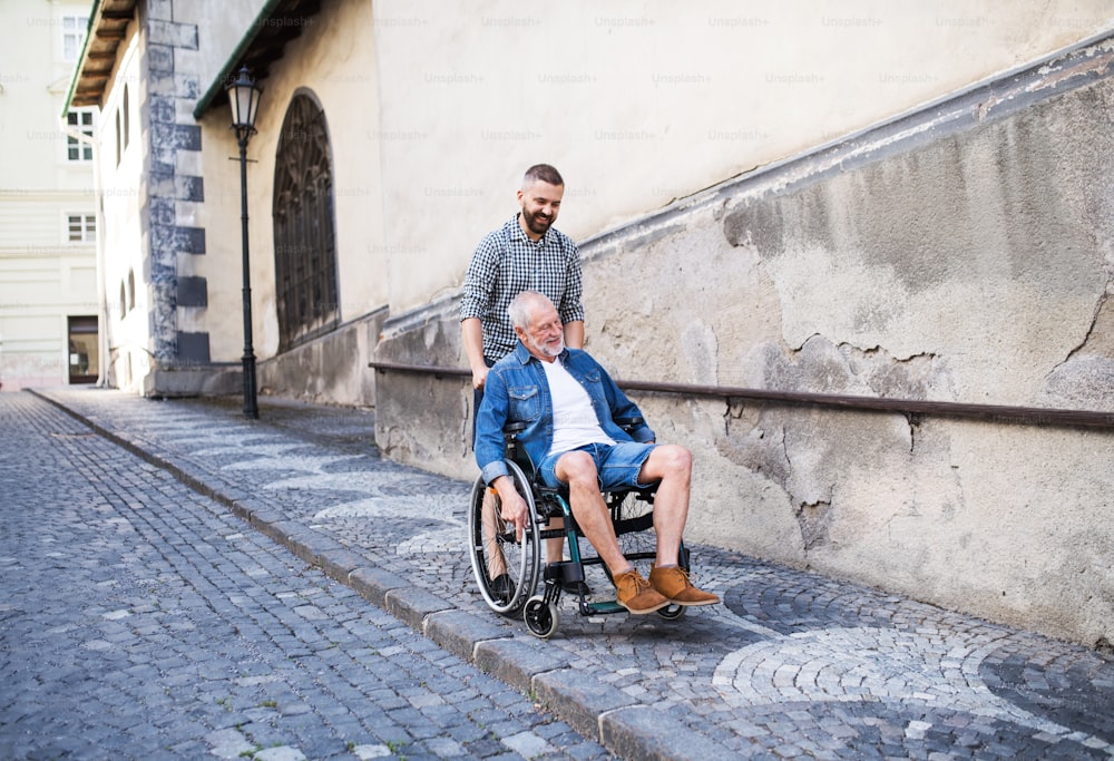 An adult hipster son with his senior father in wheelchair on a walk in town.