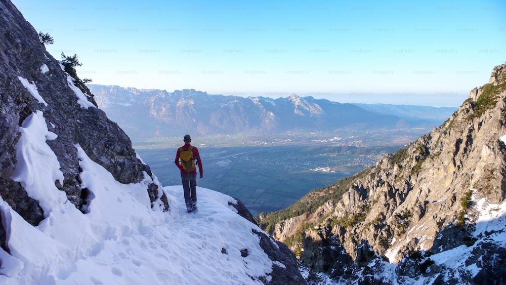 männlicher Wanderer auf einem Wanderweg im Frühwinter in den Bergen Liechtensteins mit tollem Blick auf das Rheintal unter ihm