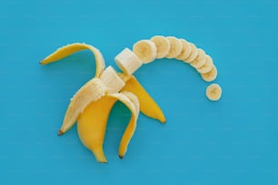 鮮やかな青い紙にバナナのスライス、トレンディなフルーツのモダンなフラットレイ。ジューシーなビタミンの抽象的な背景。食べる時間とダイエットのコンセプト。ポップアートスタイル。バナナのパターンを開いてスライス