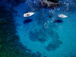 Aerial shot of beautiful blue lagoon at hot summer day with sailing boat. Top view of people are swimming around the boat.