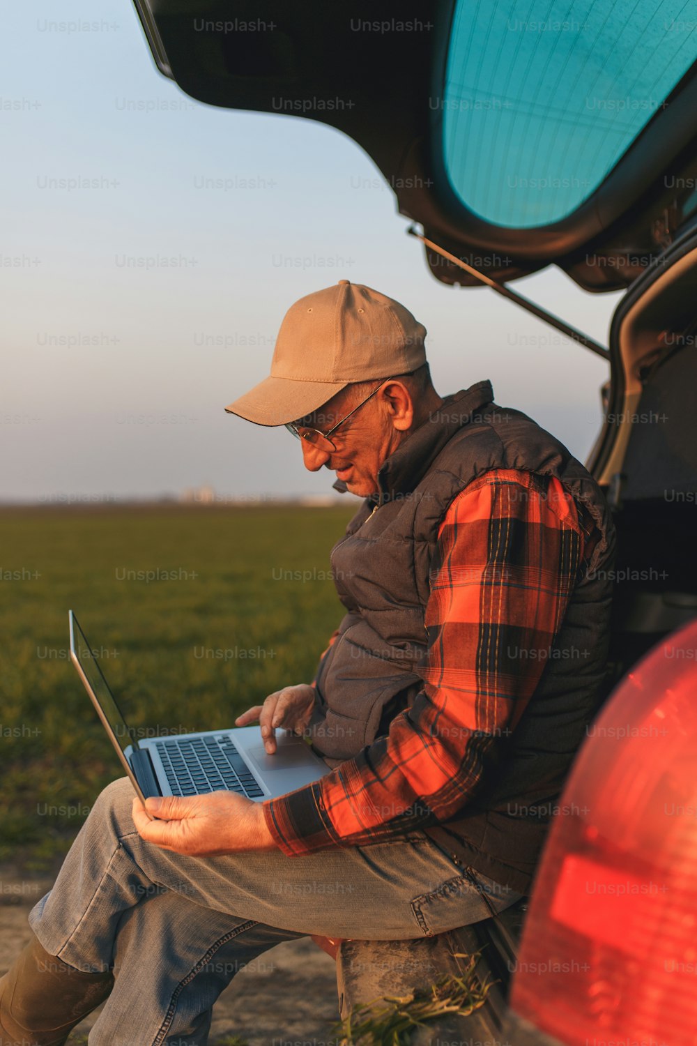 Senior farmer standing in young wheat field with laptop and examining crop.