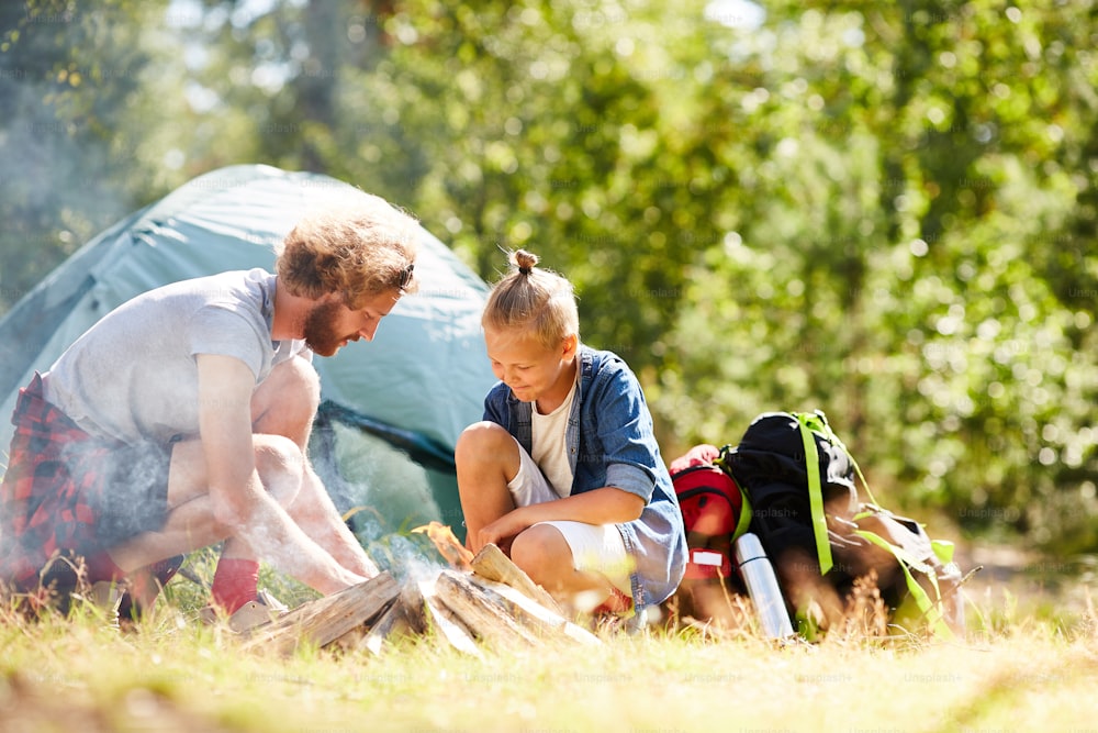 Father and son burning campfire in natural environment during trip on summer day