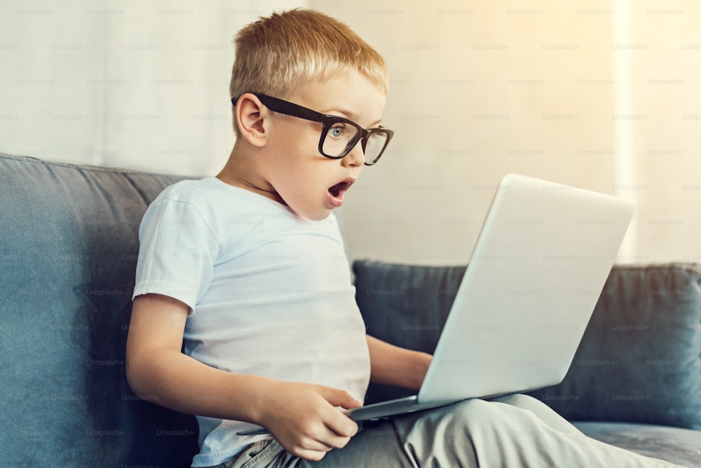 Überraschender Moment. Extrem überraschtes Kind mit großer Brille schaut auf den Bildschirm seines neuen Laptops