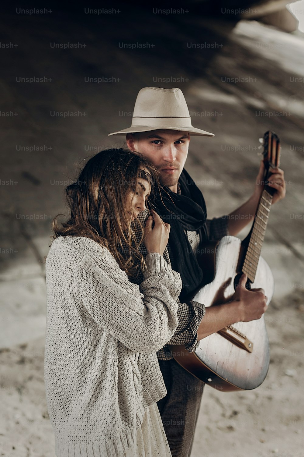 美しいヒップスターのカップル、ハンサムなカウボーイの男のギターミュージシャンと自由奔放に生きる女性は屋外でポーズをとっています