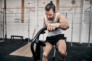 Fit young man in sportswear focused on riding a stationary bike during a workout session at the gym