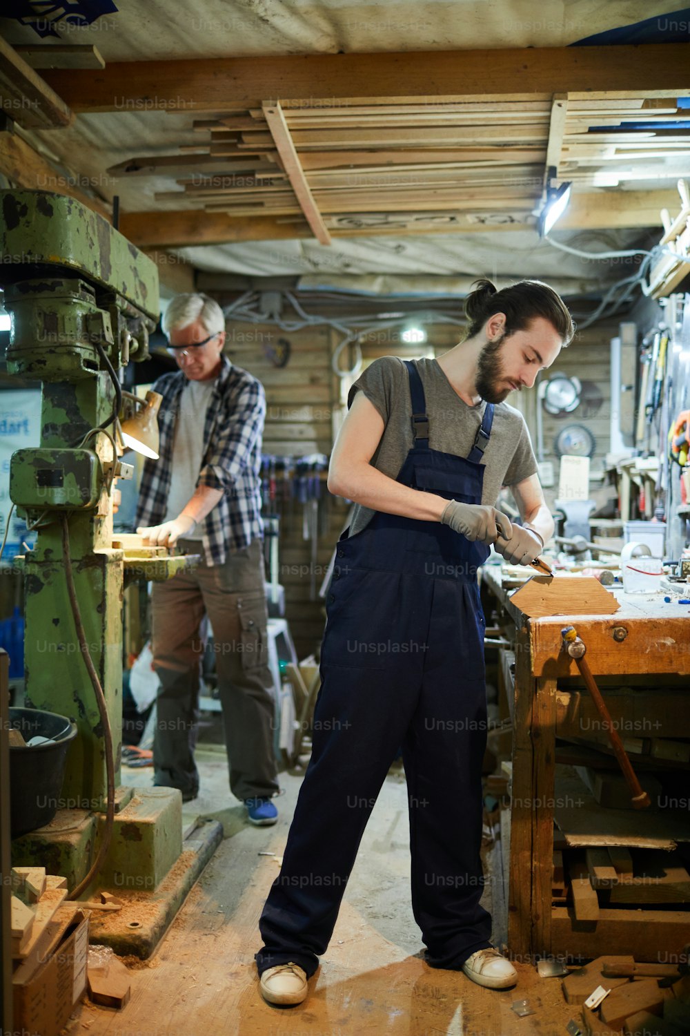 Dois mestres de marcenaria processando peças de madeira com ferramentas manuais e por máquina