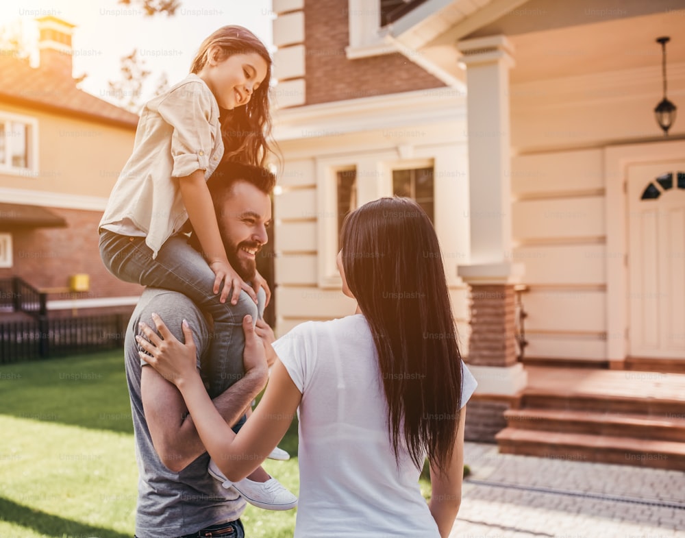 La familia feliz está de pie cerca de su casa moderna, mirándose y sonriendo.