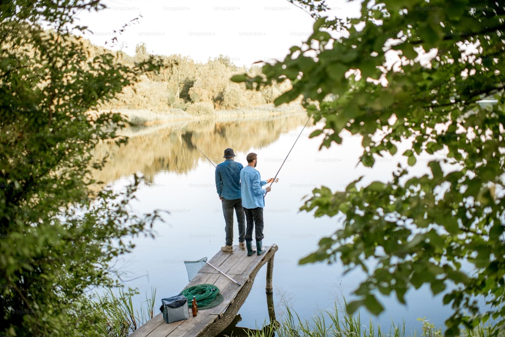 美しい湖に浮かぶ朝の光の中、木製の桟橋に立って一緒に釣りをする2人の男友達