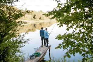 Two male friends fishing together standing on the wooden pier during the morning light on the beautiful lake