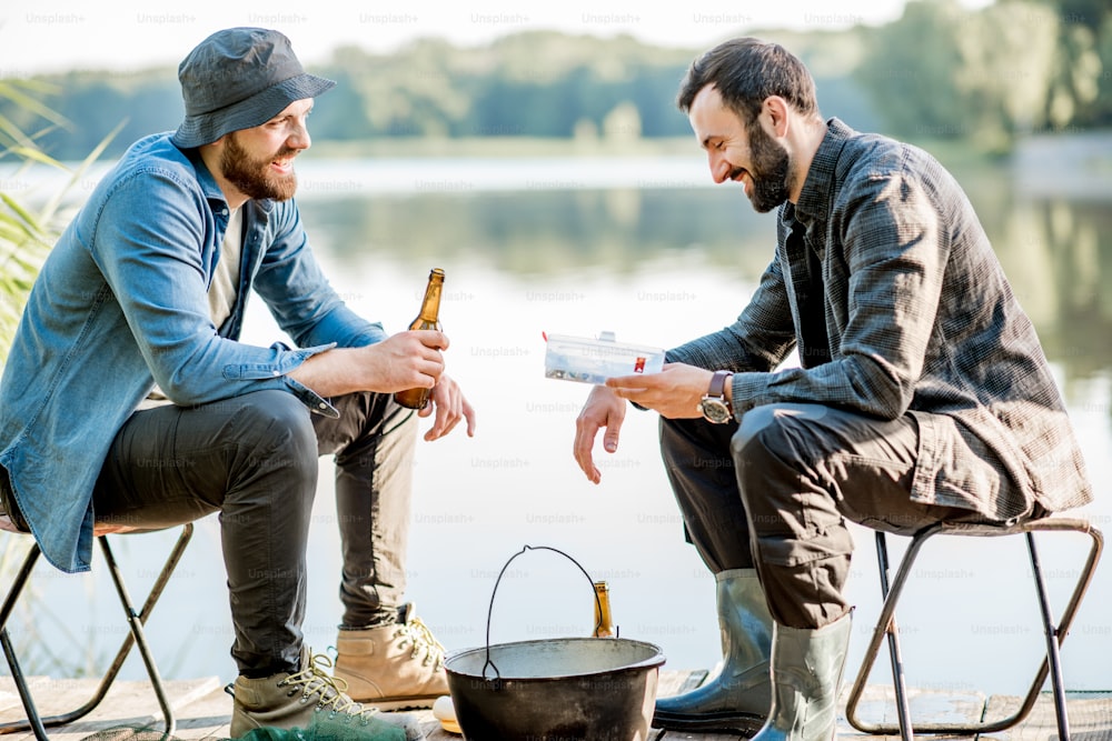 Zwei Fischer sitzen morgens beim Fischen auf dem See mit Bier zusammen