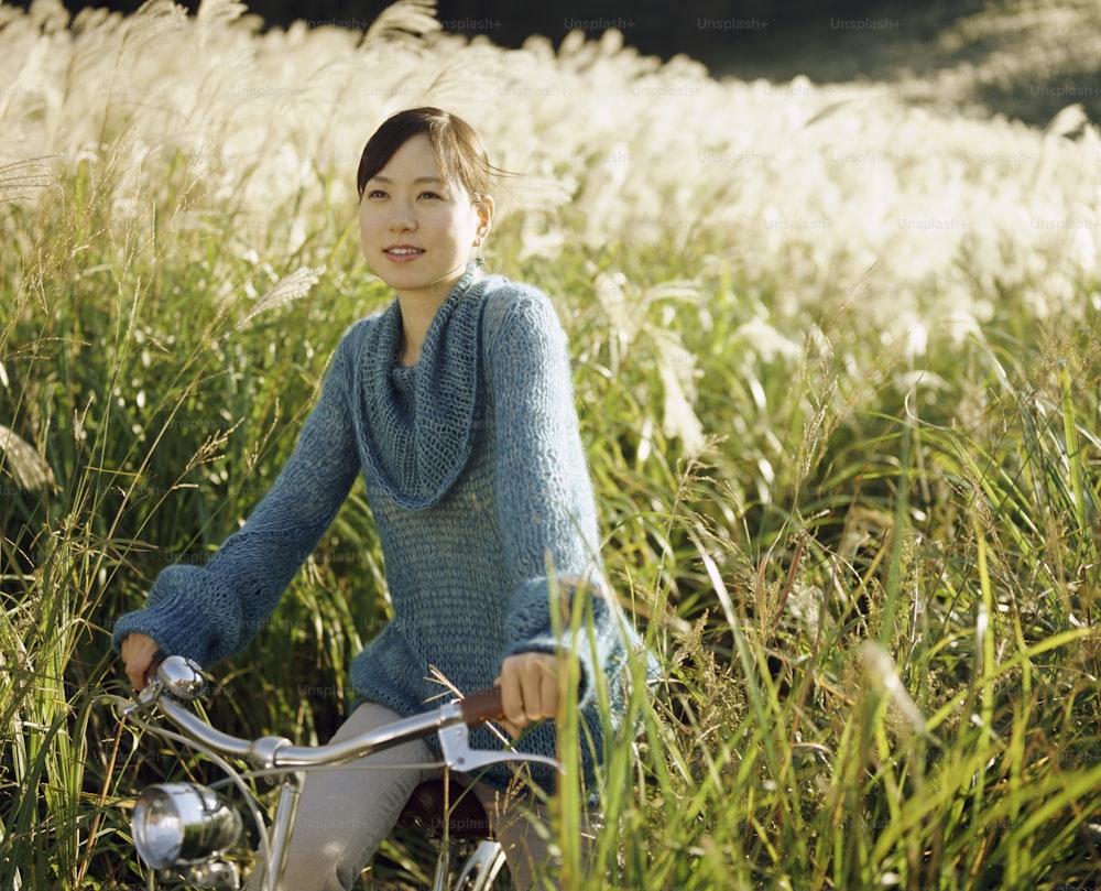uma mulher sentada em uma bicicleta em um campo de grama alta