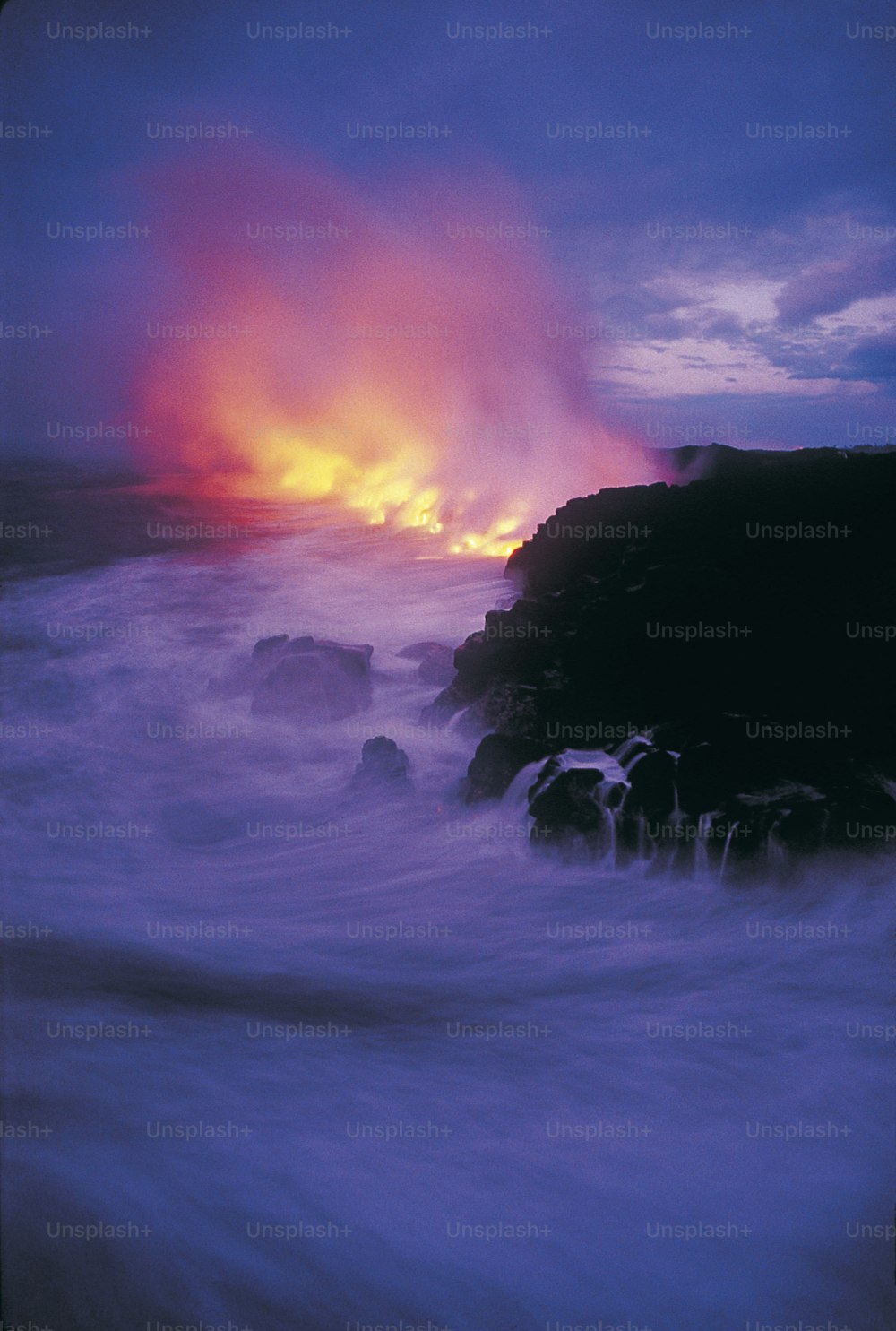 the sun is setting over the ocean with rocks in the foreground