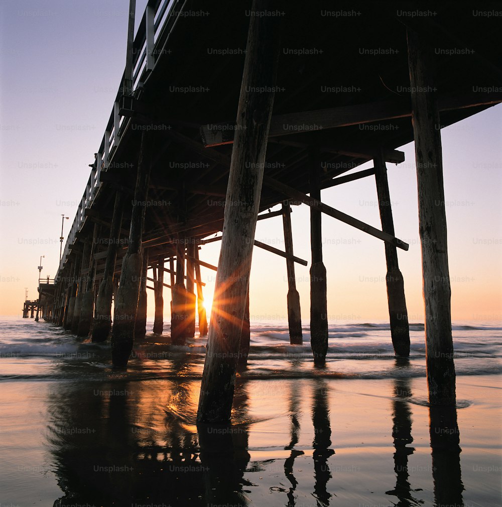 the sun is setting at the end of a pier