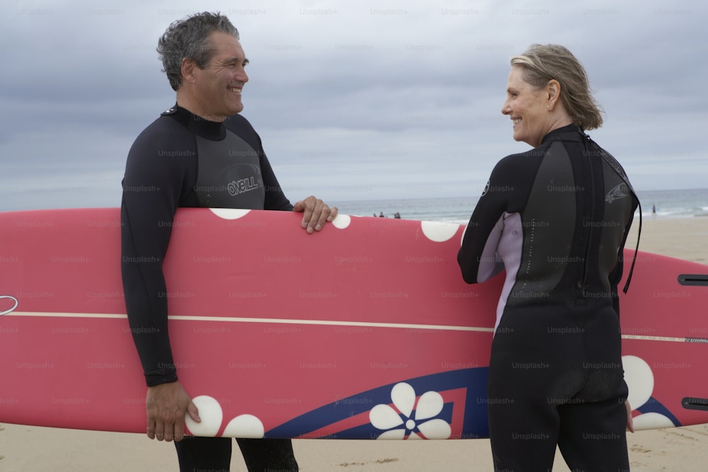 a man and a woman holding a surfboard on a beach