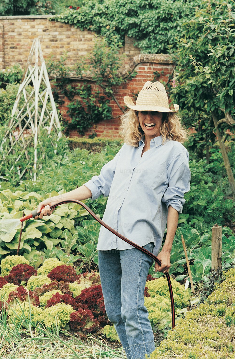 a woman in a straw hat holding a garden hose