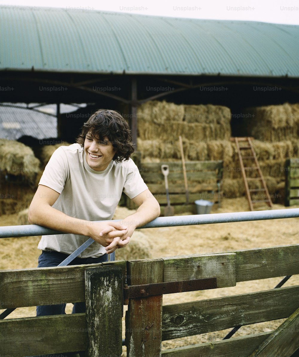 a man leaning on a fence in front of hay bales