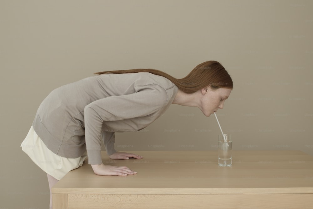 Una donna appoggiata su un tavolo che beve un bicchiere d'acqua