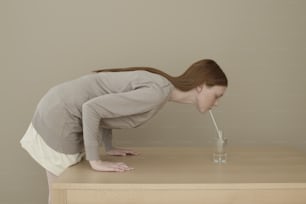 uma mulher debruçada sobre uma mesa bebendo um copo de água