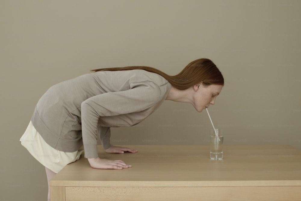 a woman leaning over a table drinking a glass of water
