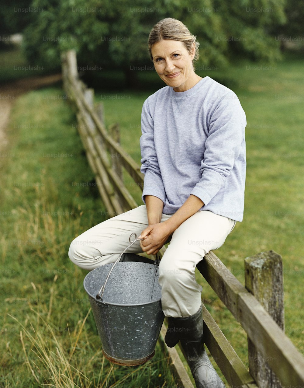 a woman sitting on a wooden fence holding a bucket